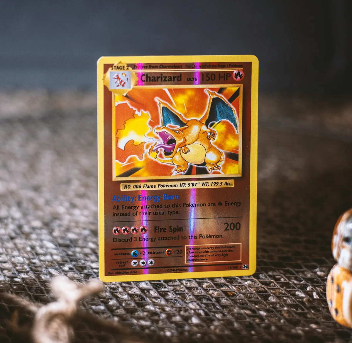A holographic trading card photographed on a dark textured surface