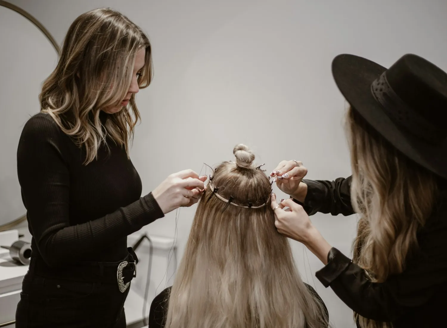 Two stylists sectioning and fitting hair extensions for a client in a salon