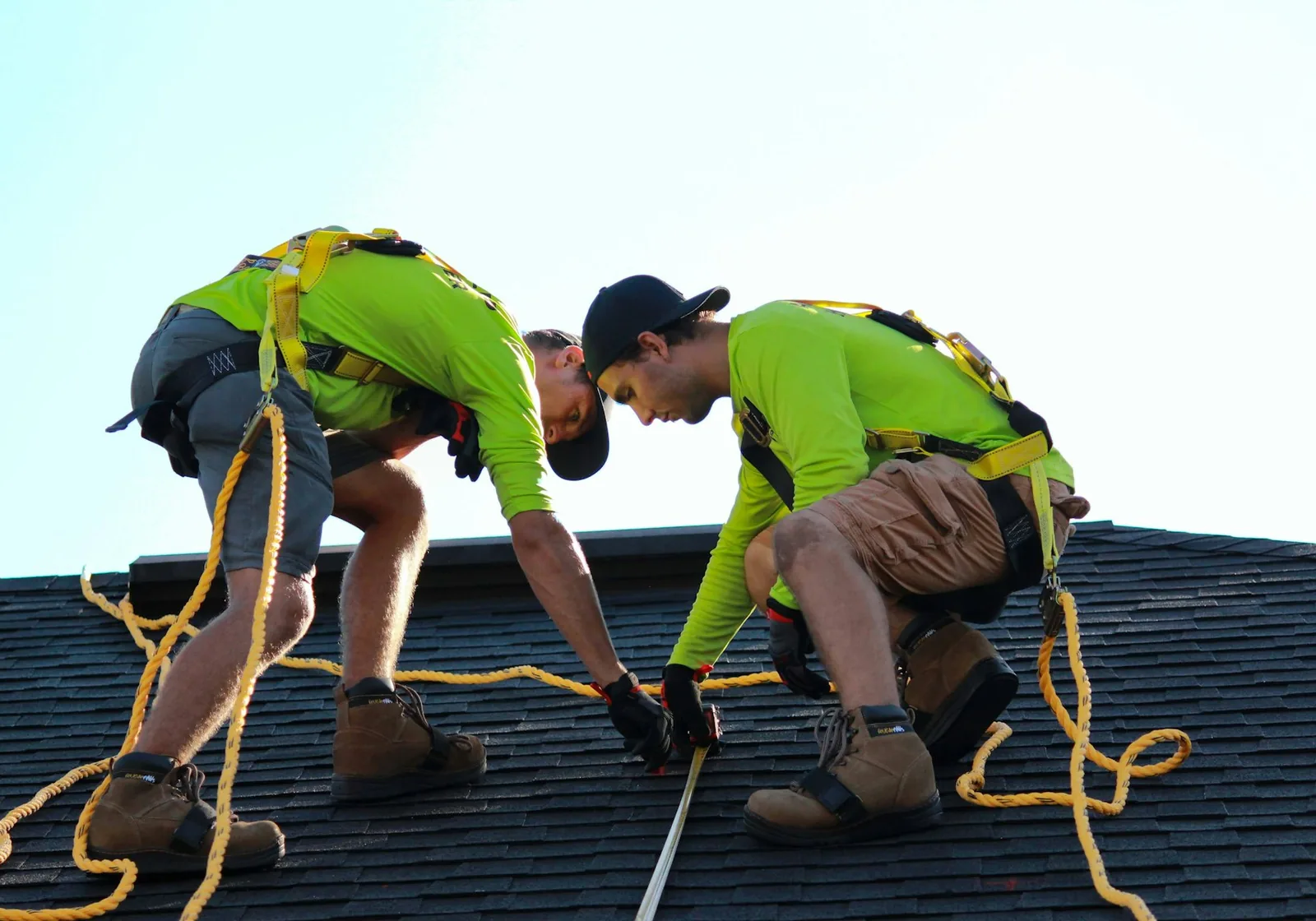 Two roofers fastening shingles on a residential roof against a clear sky