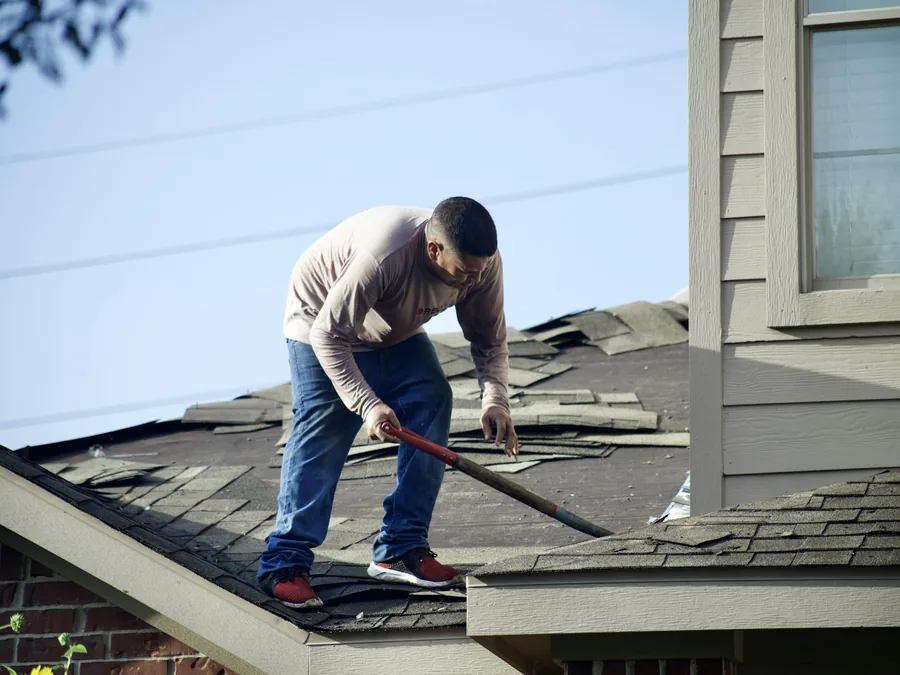Roofer stripping damaged shingles during a roof repair