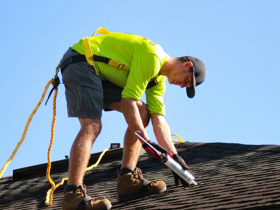Roofer fastening asphalt shingles on a new roof